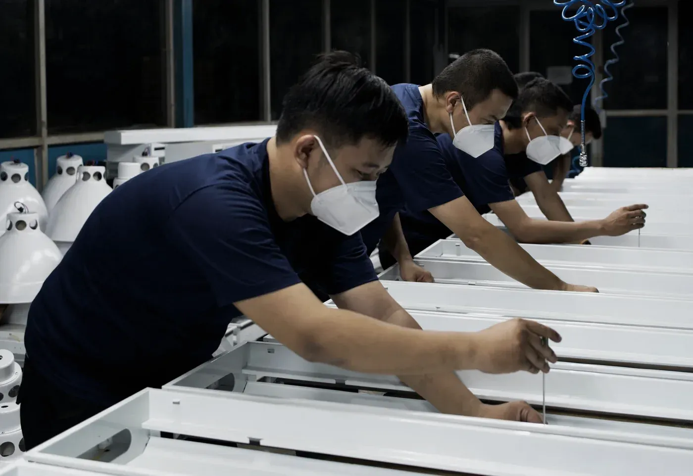 Three workers assembling white lighting fixture housings on the Metosu production line
